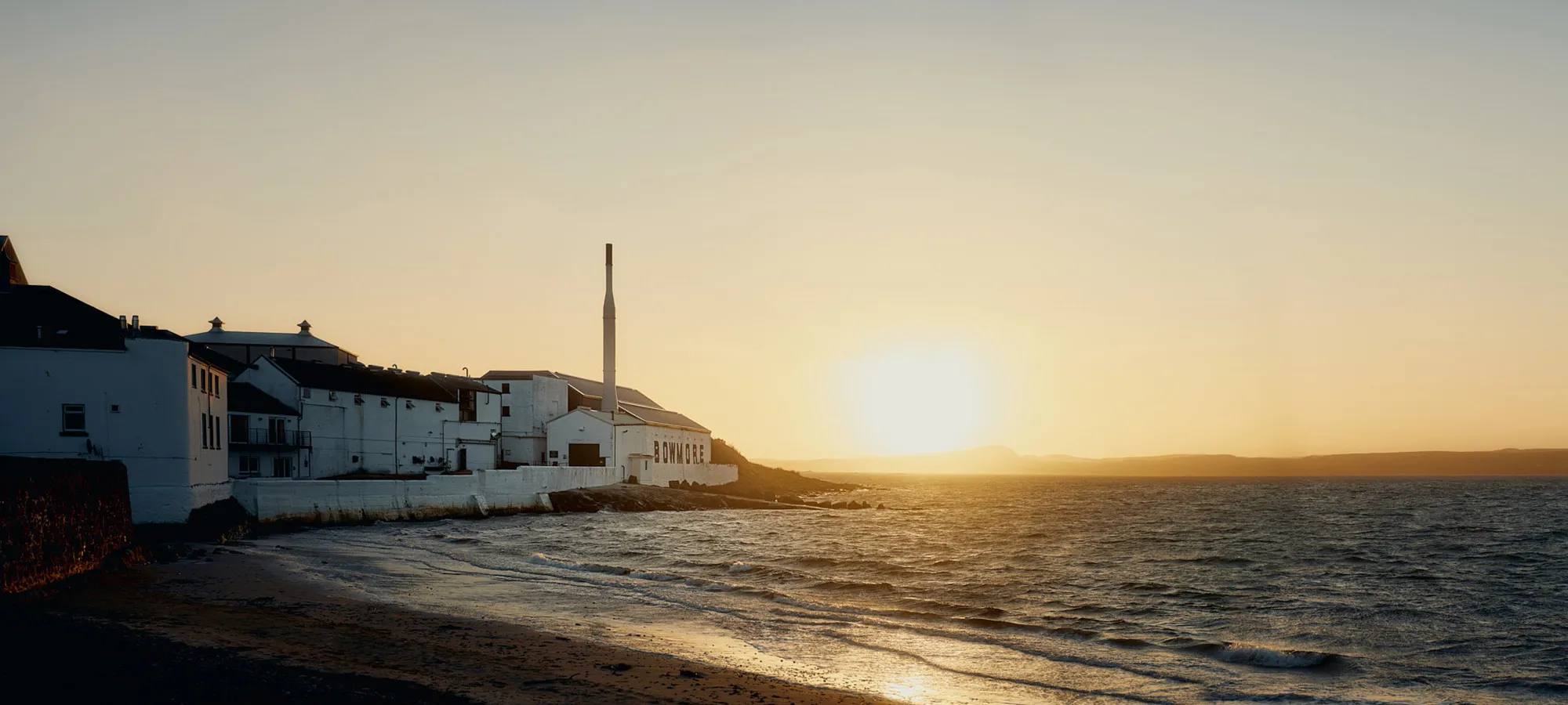 Islay distillery at dusk with loch in foreground.